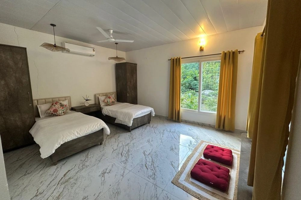 A bright twin room with marble floors, warm curtains and meditation cushions
