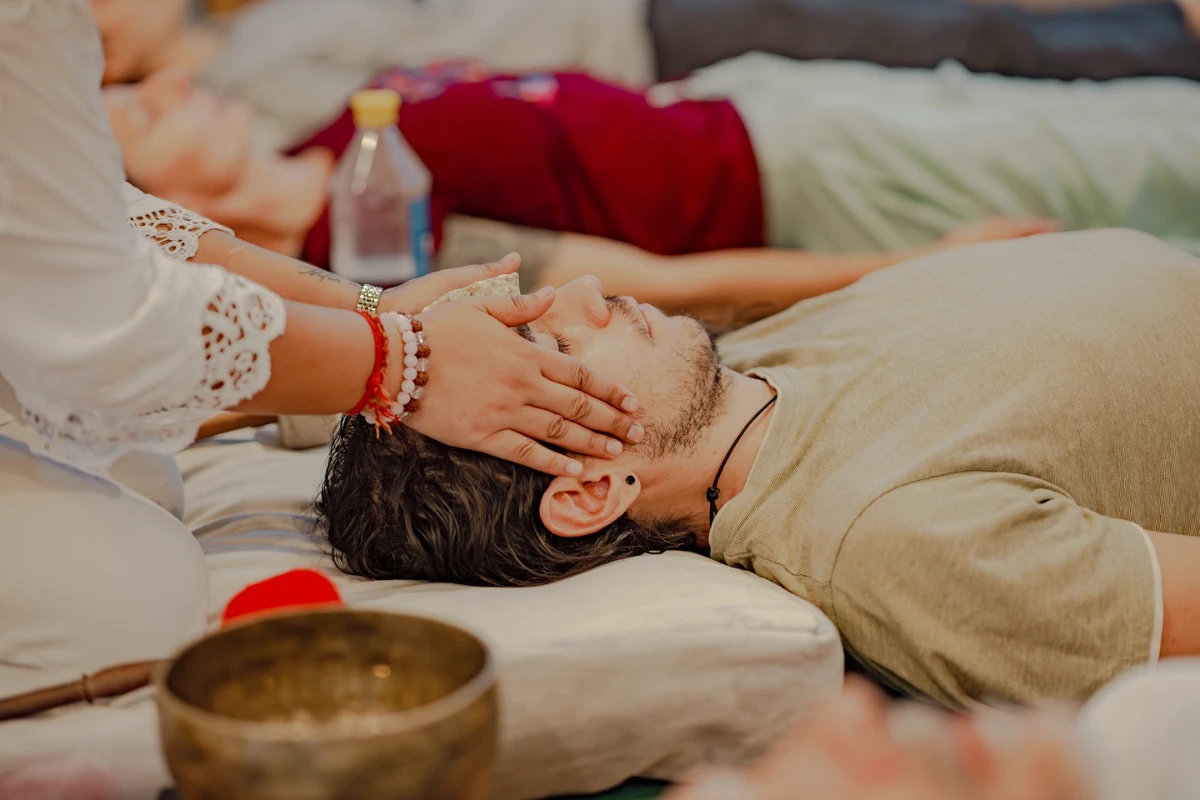 Die Hände eines Heilers stützen sanft den Kopf eines Schülers während der Klangtherapie